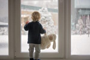 small-child-holding-stuffed-rabbit-looks-out-window-at-snow