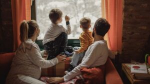 mom-dad-two-kids-look-out-window-at-snow